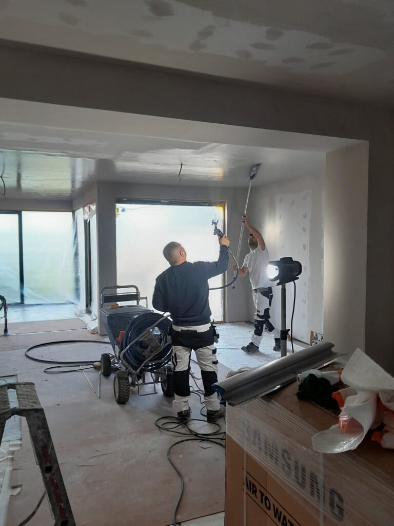 Twee vakmannen van GG Works brengen spuitplamuur aan op gyprocwanden en plafond